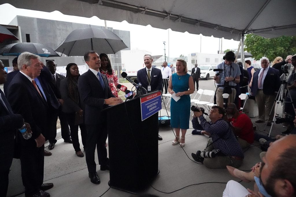 U.S. Secretary of Transportation Pete Buttigieg addresses a crowd from the podium at a press conference at the Emerson Park Transit Center