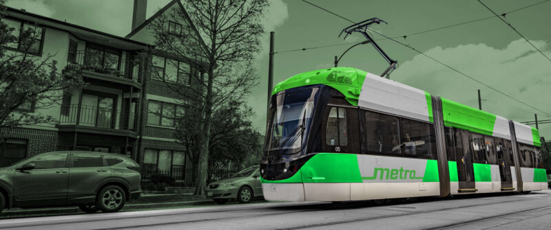 3D rendering of a street-level MetroLink train, stylized in green including a green MetroLink vehicle.