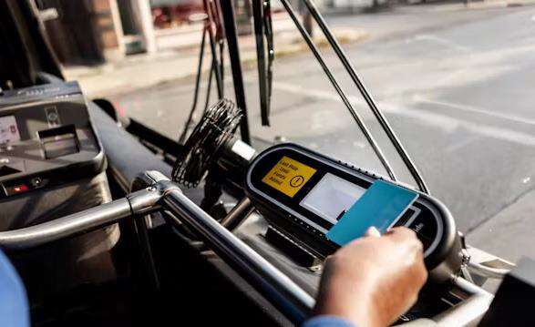 A bus passenger taps a smart payment card onto a fare validator positioned just inside a bus entrance